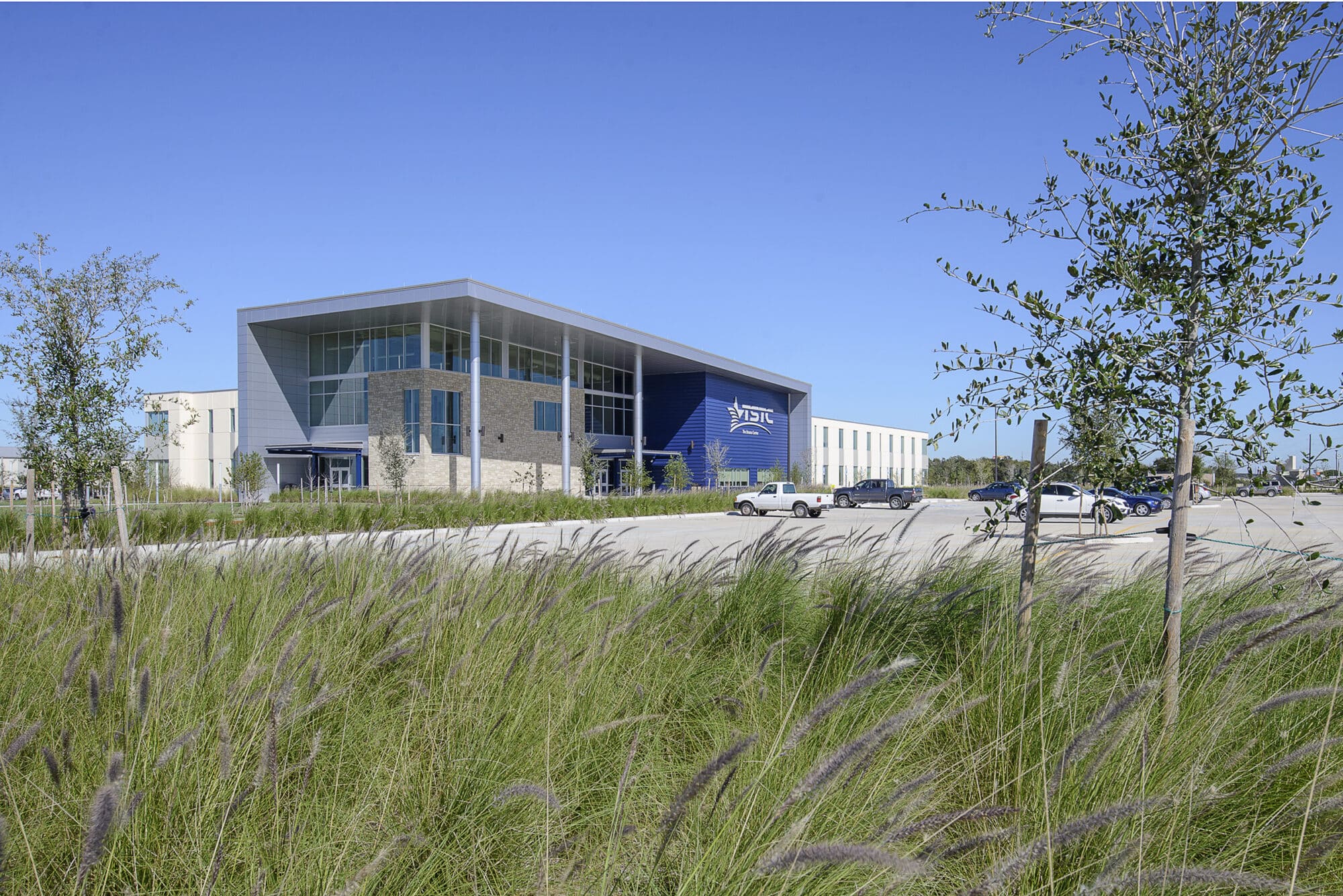 Modern industrial facility with blue logo, vehicles, clear sky.