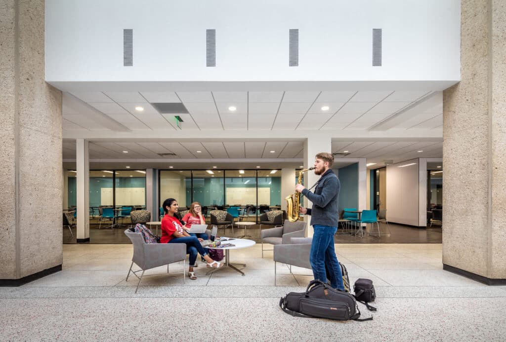 Man playing saxophone for seated women in office lobby.