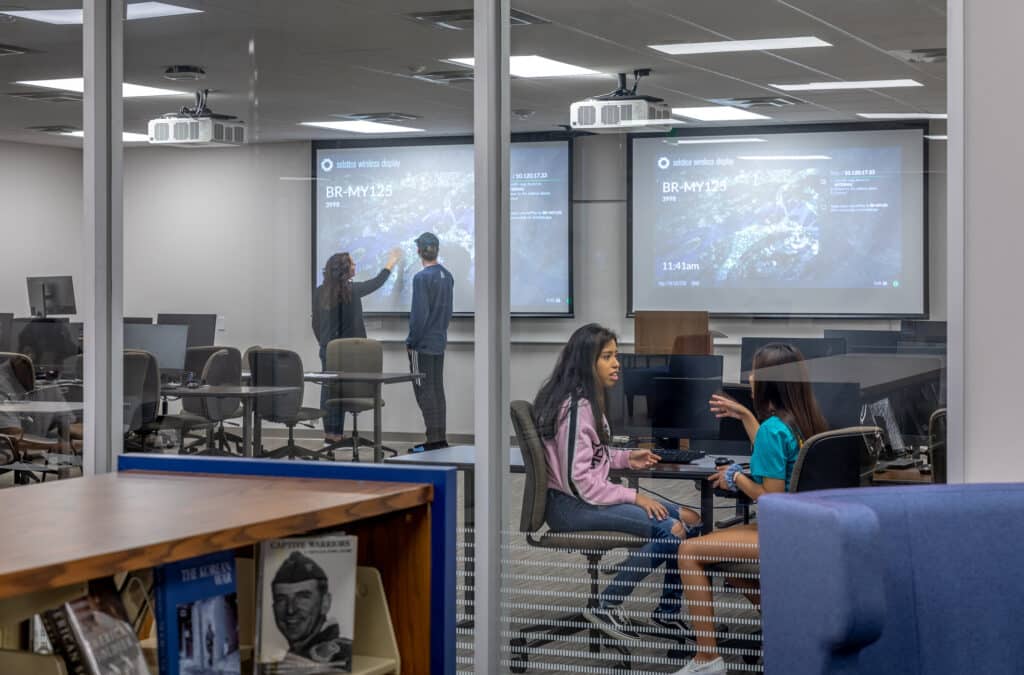 Students collaborating in modern classroom with dual screens.