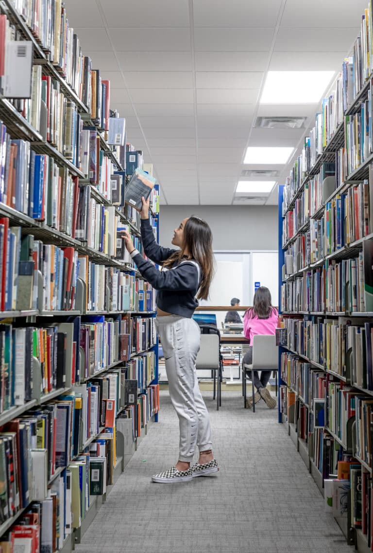 Woman browsing books in library aisle.