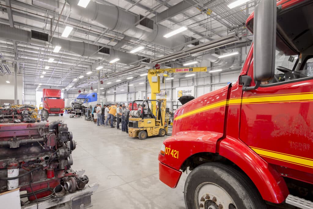 Mechanics working in vehicle repair shop with forklift.