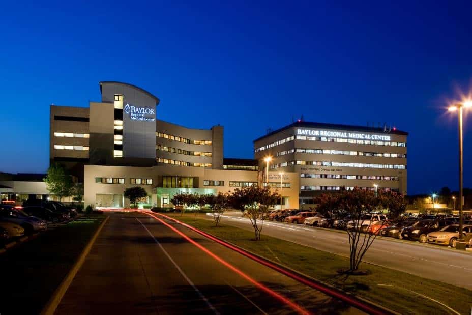 Illuminated hospital building at dusk with parking.