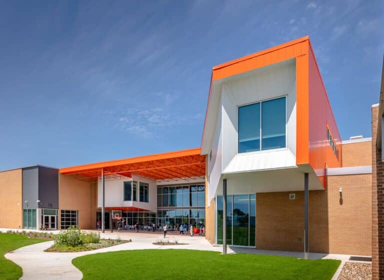Modern school building with orange accents under blue sky.