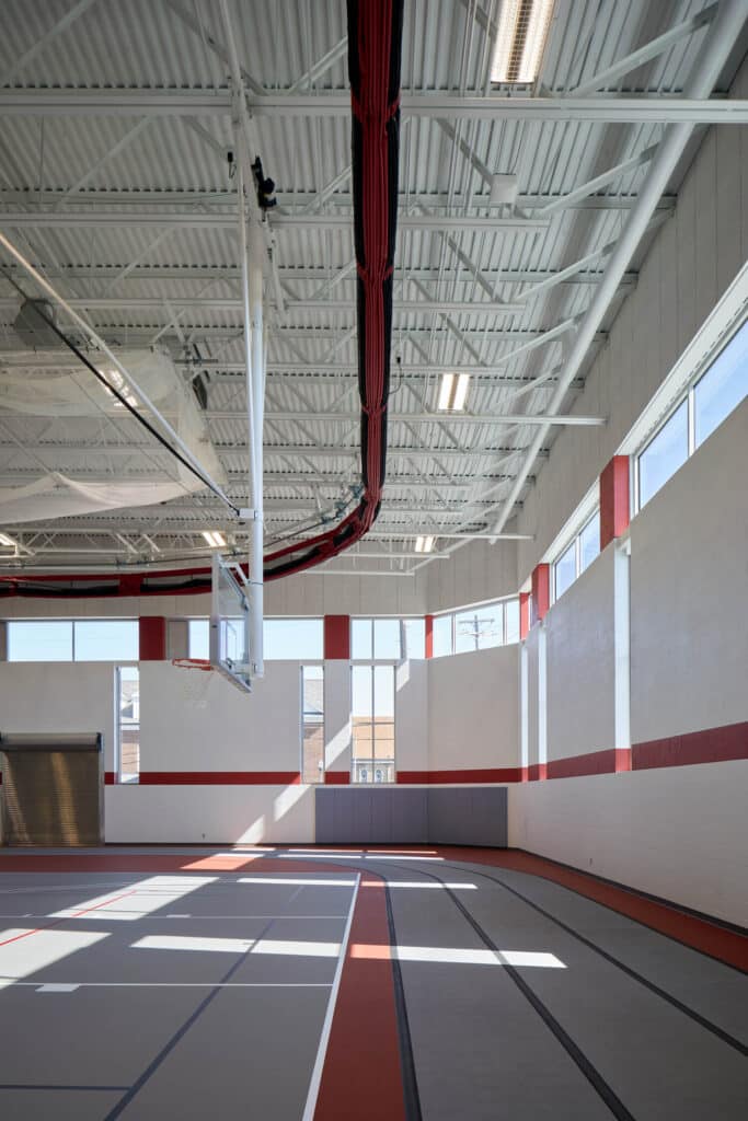 Indoor basketball court with red accents and natural light.