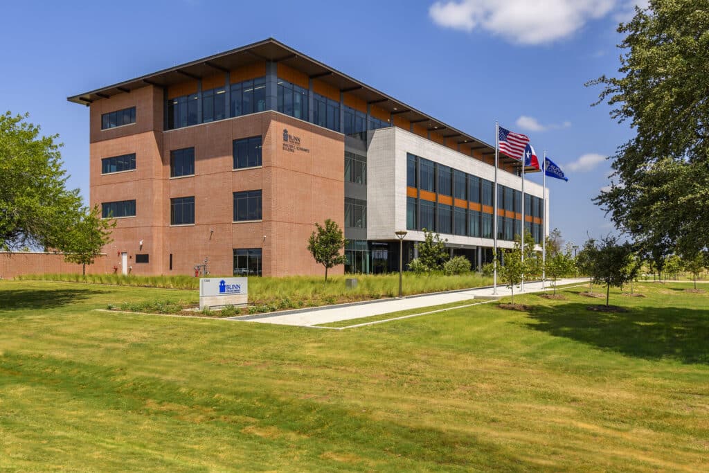 Modern campus building with flags and landscaped lawn.