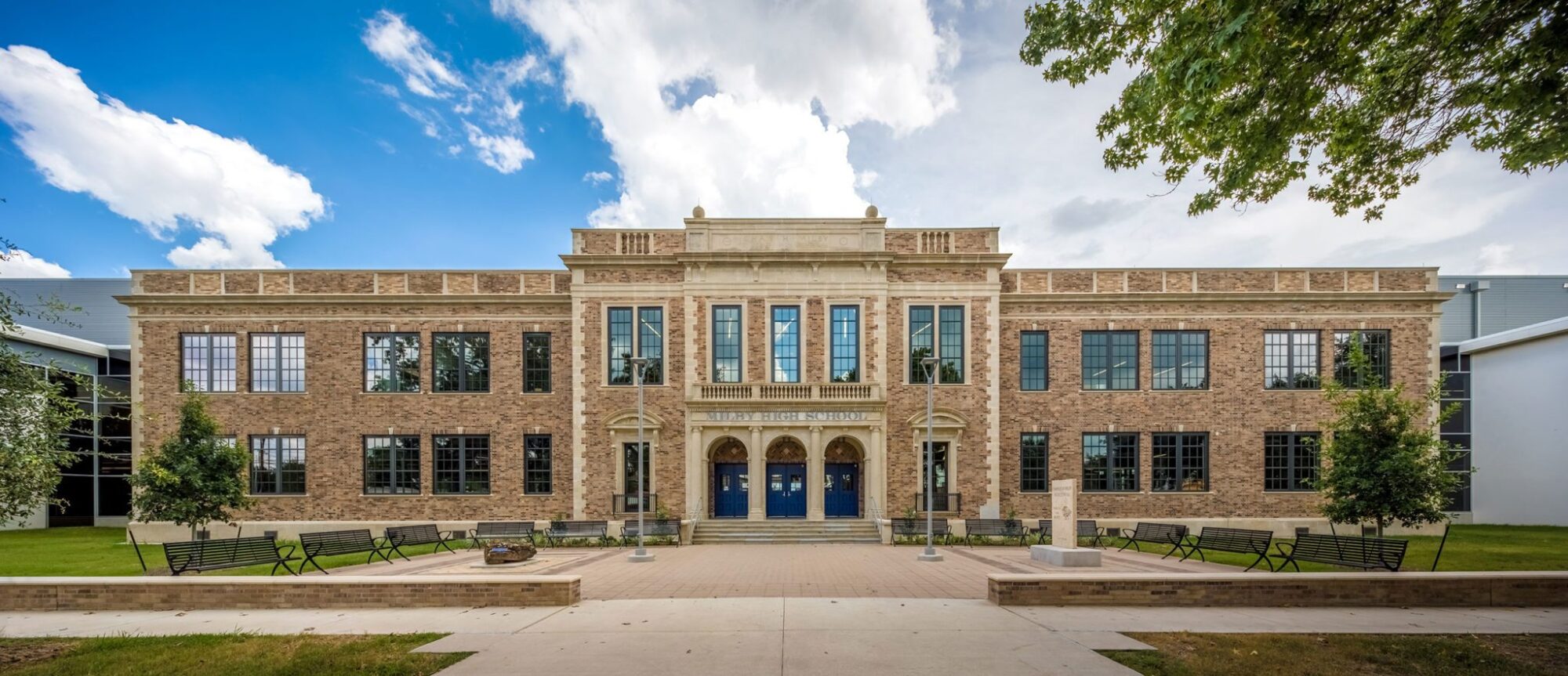 Historic high school building entrance with benches and lawn.