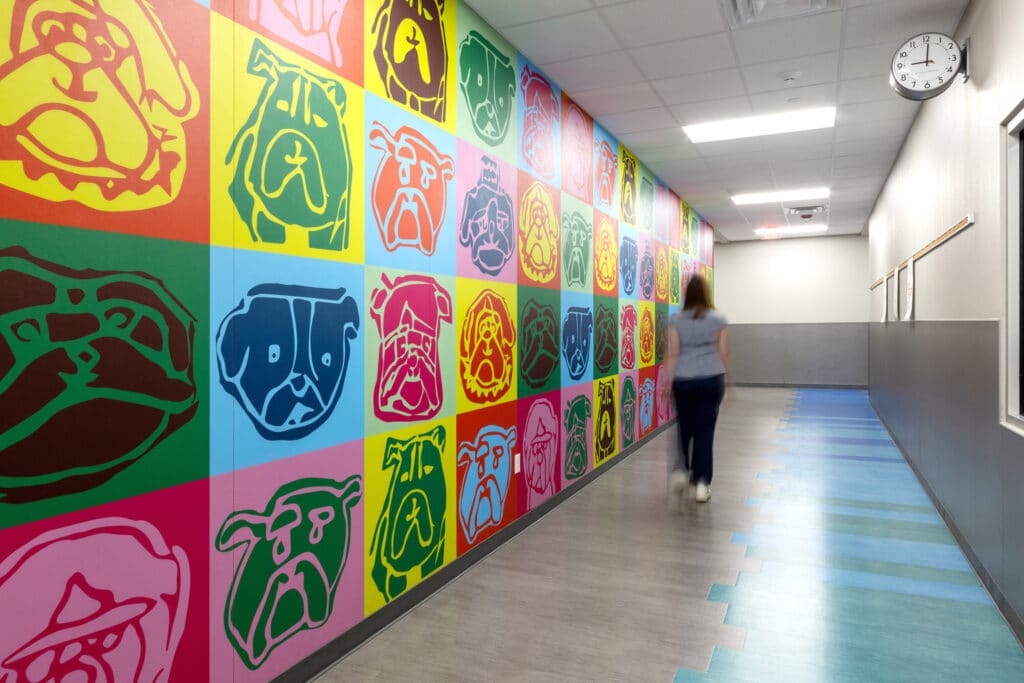 Colorful dog portraits on hallway wall with walking person.