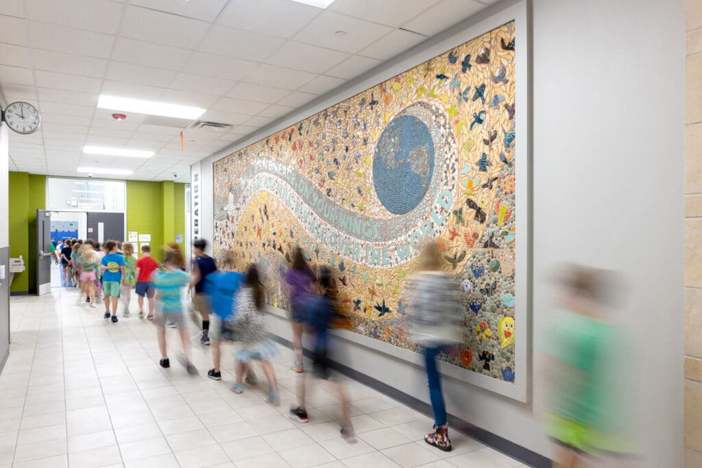 Children walking by a colorful mosaic wall in school.
