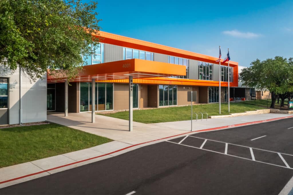 Modern office building with orange accents and parking lot.